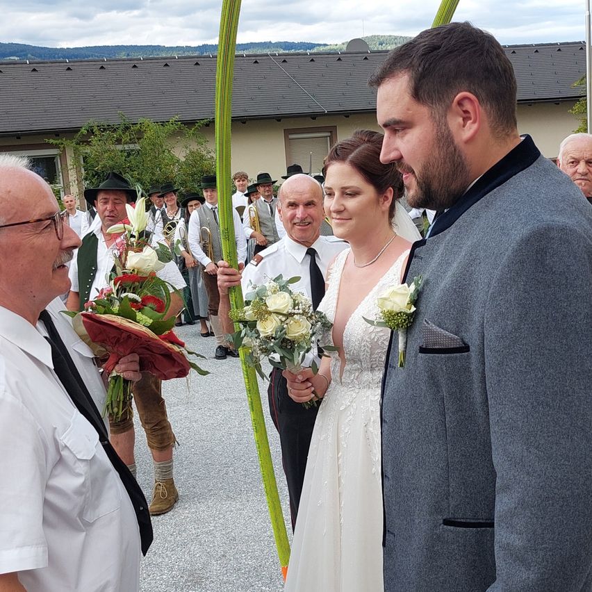 A wedding ceremony with the bride and groom standing in front of a building, a man holding flowers, and others in traditional attire.