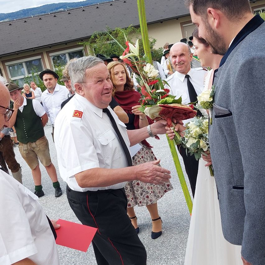 A wedding ceremony with a man in uniform presenting flowers to the bride and groom.