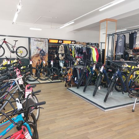 Ein Fahrradgeschäft mit einer Vielzahl von Fahrrädern, Kleidung und Zubehör. Die Fahrräder sind auf einem Holzboden ausgestellt.