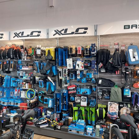 Ein Fahrradgeschäft mit einer Vielzahl von Fahrradzubehörteilen zur Schau, darunter Helme, Taschen und Fahrradteile. Die Regale sind mit Artikeln wie Reifen, Sitztaschen und anderem Zubehör gefüllt.