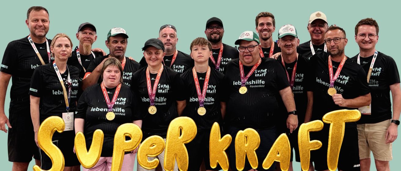 A group of people wearing matching black shirts and medals, with 'Super Kraft' written on the front. They are standing together in front of a turquoise background with gold letters reading 'Super Kraft'.