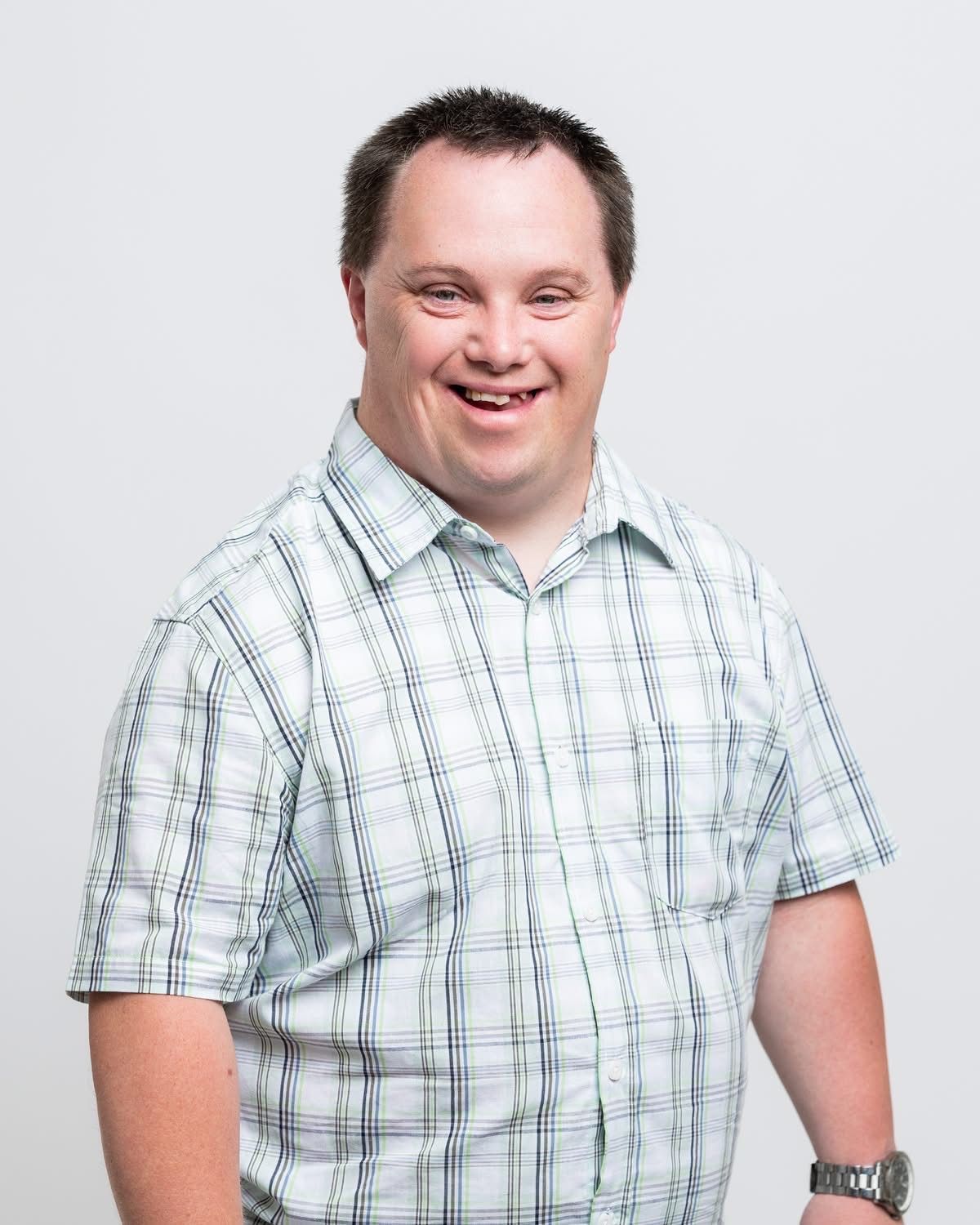 Ein lächelnder Mann in einem karierten Hemd steht vor einem weißen Hintergrund.