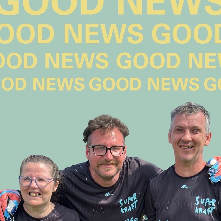 Three people in black t-shirts with the text 'Super Kraft' on them stand together against a teal background with yellow text reading 'Good News'. The man in the middle wears glasses and a mustache.
