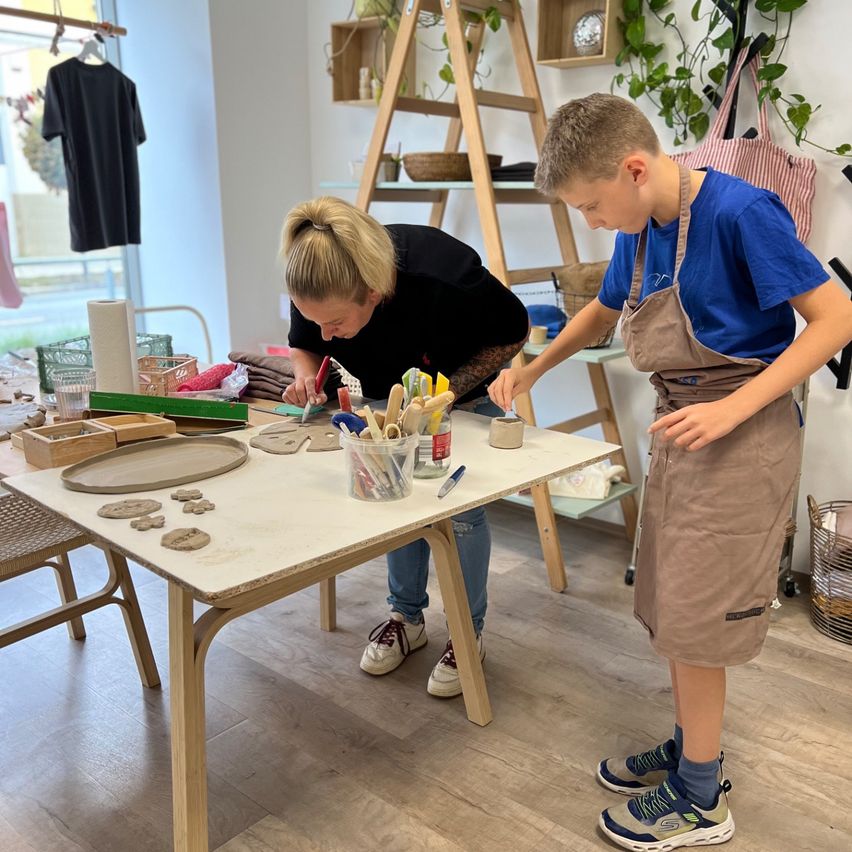 Eine Frau und ein Junge arbeiten in einer Werkstatt an einem Bastelprojekt am Tisch.