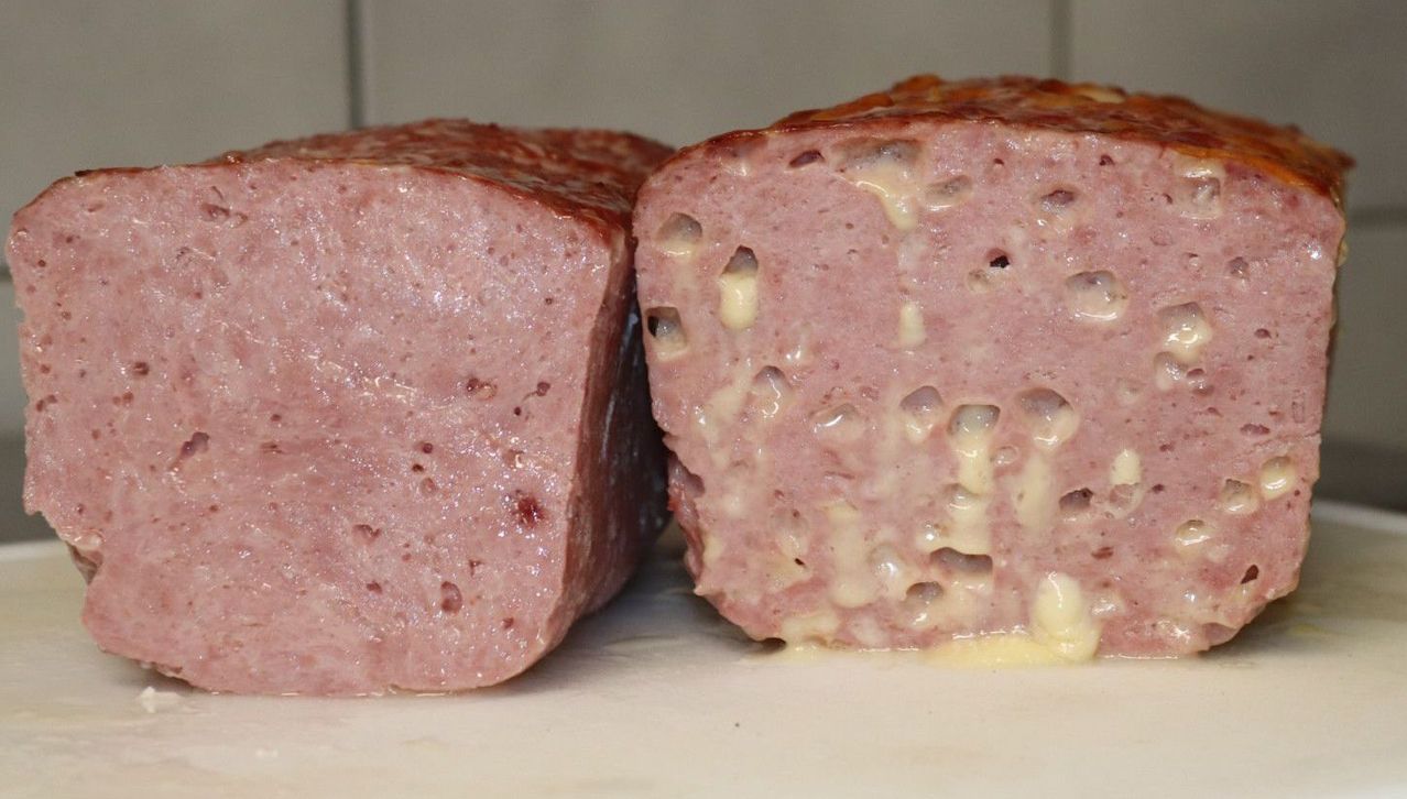 Two slices of pink meat with white spots, possibly cheese, are on a white surface. The meat has a slightly glossy texture.