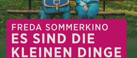 Ein älterer Mann und eine Frau sitzen auf einer Parkbank und halten Händchen. Der Mann trägt eine Brille und einen Rucksack. Die Frau trägt einen blauen Pullover. Ein rosa Banner mit weißem Text lautet 'Freda Sommerkino Es sind die kleinen Dinge'.