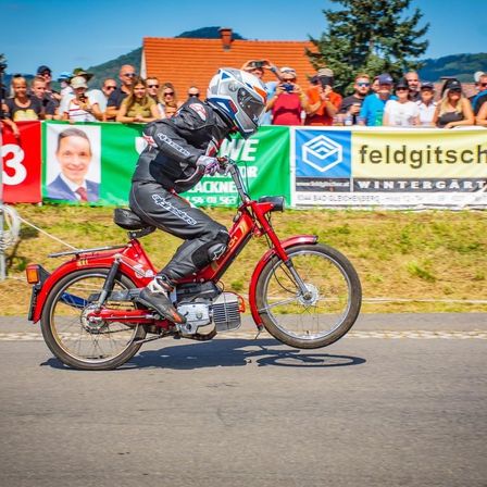 Eine Person, die mit einem Helm auf dem Kopf auf einem roten Motorrad vor einer Menge fährt.