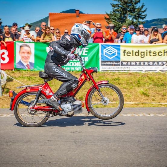 Eine Person, die mit einem Helm auf dem Kopf auf einem roten Motorrad vor einer Menge fährt.