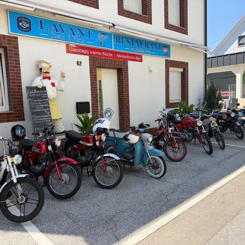 A restaurant named Lavant Steak & Fisch with a chef statue outside. Several motorcycles are parked in front of the building.