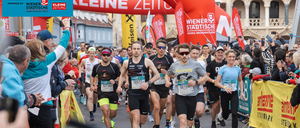 Eine große Menschenmenge nimmt an einem Marathon teil. Läufer sind in einer Reihe auf einer Straße zu sehen. Zuschauer feuern sie von der Seite an.