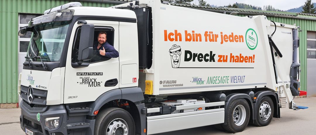 Ein weißer Lastwagen mit dem Slogan 'Ich bin für jeden Dreck zu haben!' und einem Mann am Steuer. Der Lastwagen steht auf einer Ziegelstraße.