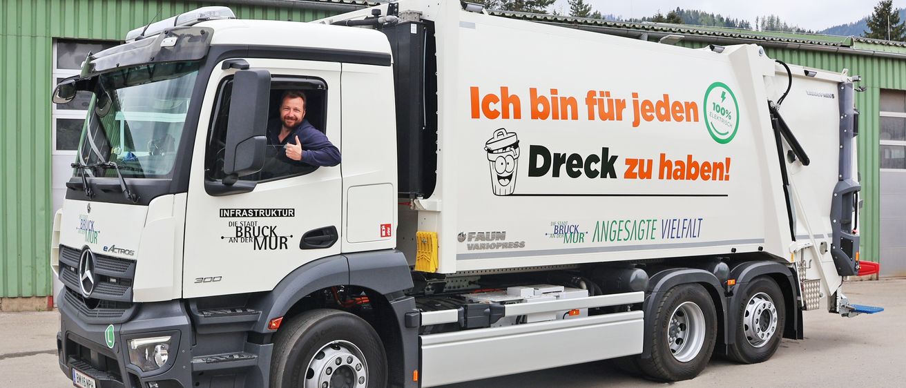 Ein weißer Lastwagen mit dem Slogan 'Ich bin für jeden Dreck zu haben!' und einem Mann am Steuer. Der Lastwagen steht auf einer Ziegelstraße.