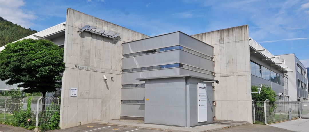 Ein modernes Gebäude mit einem Empfangsschild, großen Fenstern und einem Parkplatz unter einem klaren Himmel.