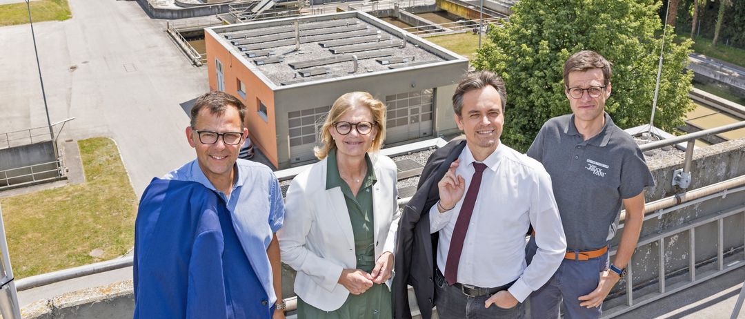 Vier Menschen stehen lächelnd vor einem Gebäude und scheinen für ein Foto zu posieren.