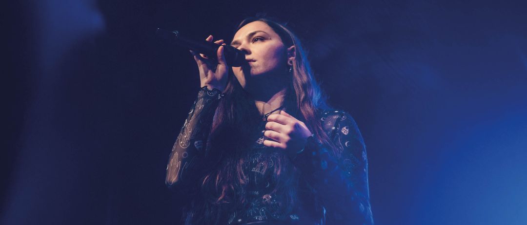 Werbeposter für 'Soundscapes', zeigt eine Sängerin auf der Bühne mit Mikrofon vor blauem Hintergrund. Der Text lautet 'Soundscapes Orchester der Musikschule von Pop bis Hip-Hop' und beinhaltet Datum und Ort.