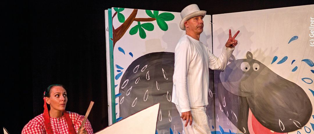 Plakat für eine Theaterveranstaltung. Zwei Darsteller sind abgebildet. Ein Mann macht ein Friedenszeichen. Eine Frau hält eine Paddel. Ein Nilpferd ist an der Wand gemalt. Datum und Uhrzeit sind angegeben: 1. Februar 2026, 16:00 Uhr.