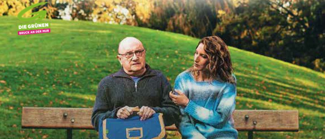 Eine Parkbank im Freien mit zwei Personen, einem Mann und einer Frau. Der Mann hält eine blaue Tasche. Die Frau hat lockige Haare. Der Text lautet Freda Sommerkino.