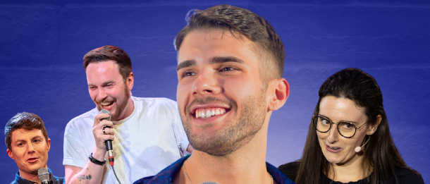 Vier Personen stehen auf einer Bühne, jede hält ein Mikrofon. Der Mann in der Mitte lächelt und hält sein Mikrofon nah an seinen Mund. Die anderen lächeln und schauen in die Kamera. Der Hintergrund ist blau.