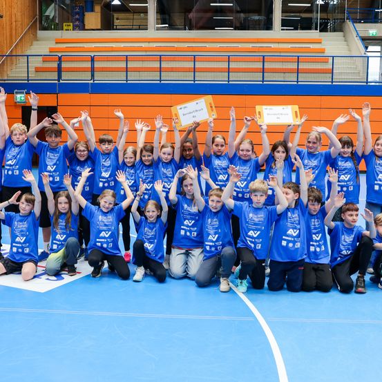 Eine Gruppe von Kindern in blauen Shirts posiert mit Urkunden auf einem Indoor-Court für ein Foto.