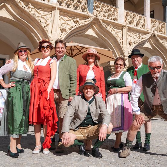 Eine Gruppe von Menschen in traditioneller bayerischer Kleidung posiert für ein Foto vor einem historischen Gebäude.