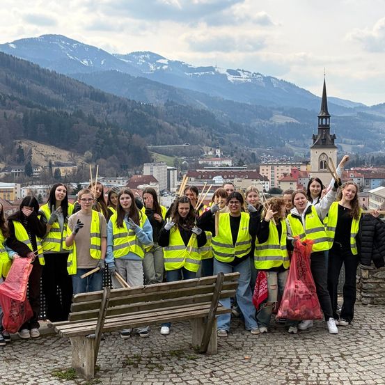 Eine Gruppe von Menschen in Sicherheitswesten posiert für ein Foto mit einer Stadt und Bergen im Hintergrund.