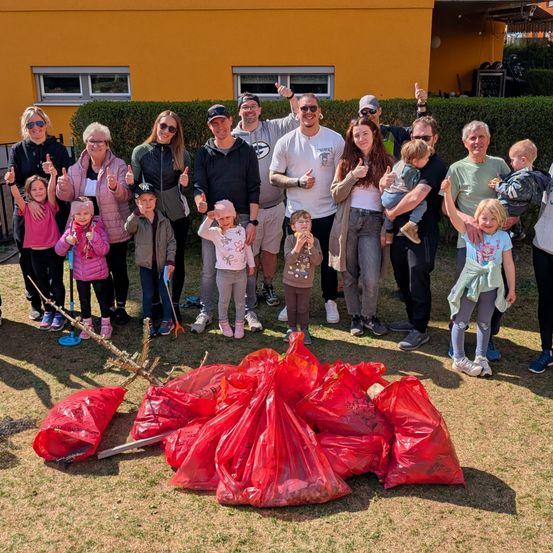 Eine große Familie versammelt sich vor einem gelben Gebäude und lächelt für ein Foto mit roten Mülltüten vor sich.
