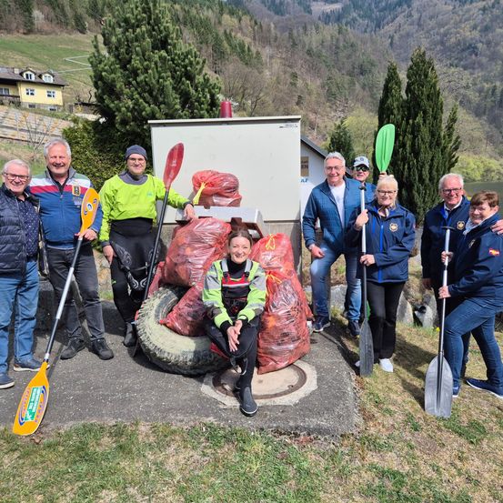 Eine Gruppe von Menschen posiert mit ihren Paddeln und Tüten voller Müll, die auf einem Reifen in der Nähe eines Berges sitzen.