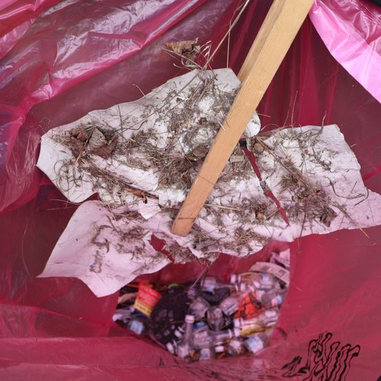 Ein Müllsack voller Müll, einschließlich Papier, Erde und Flaschen, hängt an einem Holzstab.