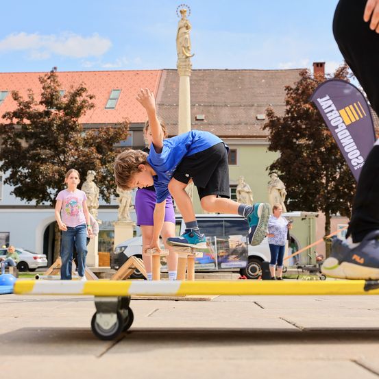 Ein junger Junge in Blau macht einen Trick auf einem Skateboard draußen auf einem Stadtplatz.