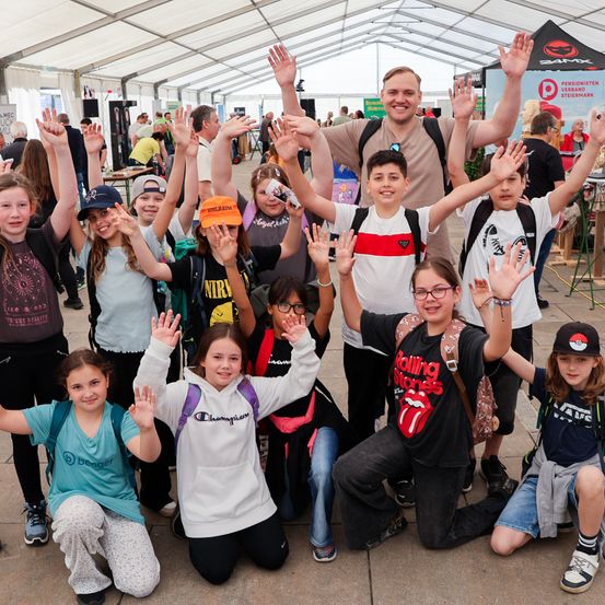 Eine Gruppe von Kindern und Erwachsenen lächelt und posiert für ein Foto in einem Zelt, wobei eine Person ein Rolling-Stones-T-Shirt trägt.