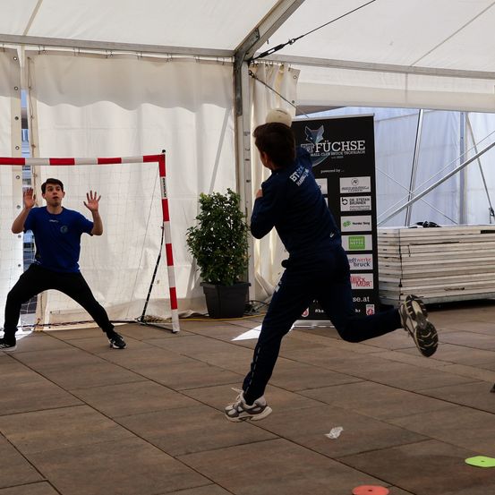 Zwei Männer spielen Volleyball unter einem Zelt. Einer serviert den Ball, während der andere sich darauf vorbereitet, ihn zu empfangen.