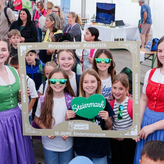Eine Gruppe von Kindern und Erwachsenen posiert für ein Foto vor einem Rahmen, der den 55. Jahrestag einer Kindergruppe feiert. Das Foto wurde im Freien aufgenommen.