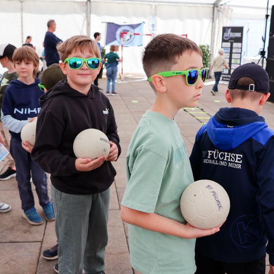 Vier Jungen in einem Sportzelt mit Fußballbällen. Zwei Jungen tragen grüne Sonnenbrillen, während andere Mützen tragen. Ein Jungen-Hemd hat den Text 'Füchse'.