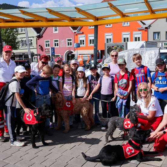 Eine Gruppe von Erwachsenen und Kindern mit Hunden in roten Westen posiert für ein Foto vor Gebäuden.