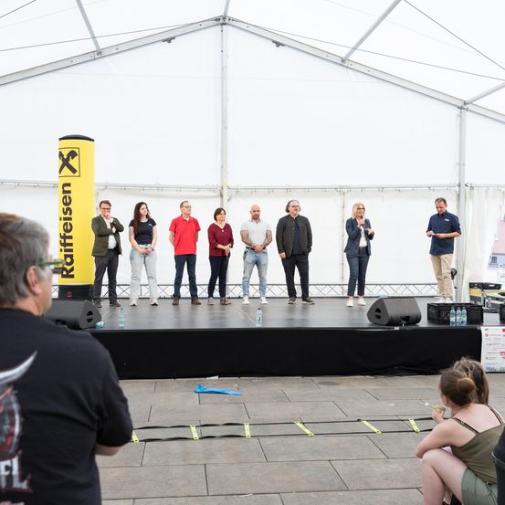 Eine Gruppe von Menschen steht auf der Bühne, mit einem gelben Schild, auf dem 'Kaffeereisen' steht. Sie stehen mit Blick auf das Publikum, mit Lautsprechern und Flaschen auf der Bühne. Ein Zuschauer sitzt unten, und andere beobachten.