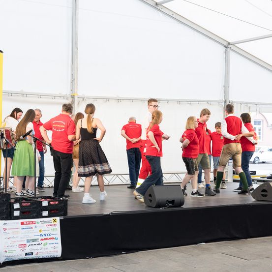 Eine Gruppe von Menschen in roten Shirts und Hosen steht auf der Bühne mit Musikinstrumenten. Sie scheinen für eine Aufführung zu proben.