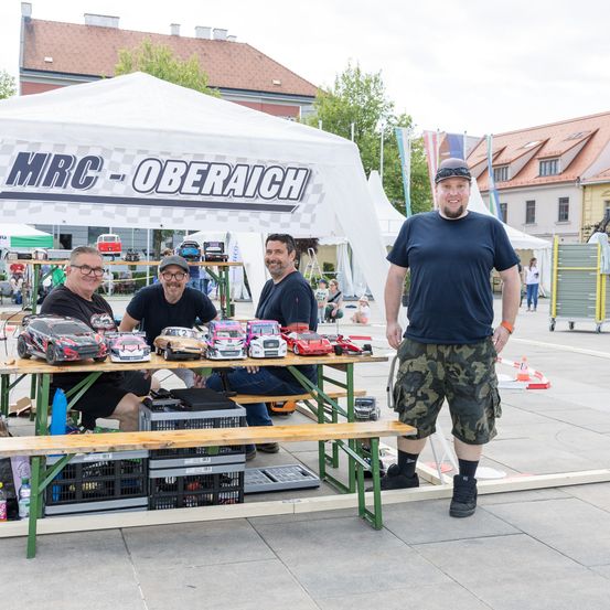 Vier Männer posieren neben einem Tisch mit Spielzeugautos unter einem weißen Zelt mit dem Wort Oberreich darauf.