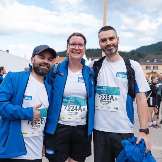 Drei Personen posieren für ein Foto bei einem Marathon-Event. Die Frau trägt eine blaue Jacke mit 'Boehringer Ingelheim' und ein Nummernband mit 'Jasmin'. Der Mann links hat ein 'Johann'-Nummernband. Der Mann rechts hat ein weißes T-Shirt mit 'Johannes' und einem 'Boehringer'-Logo.