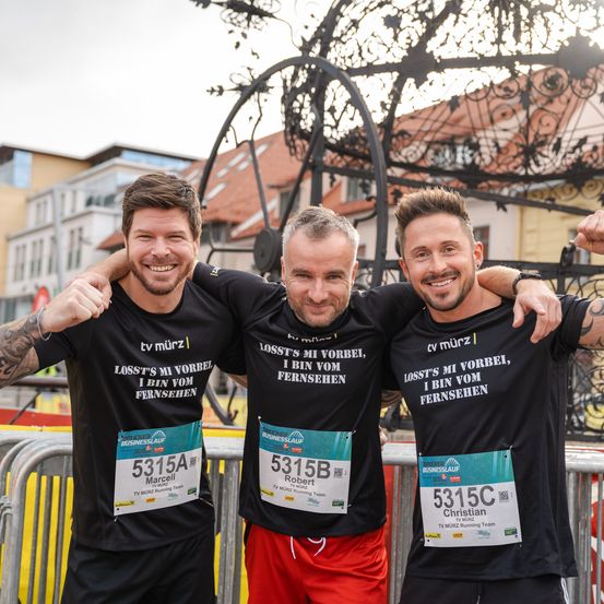 Drei Männer posieren für ein Foto bei einem Marathon, alle tragen schwarze T-Shirts mit dem Slogan 'Ich vermisse meinen Fernseher' und ihre Startnummern. Der Mann auf der linken Seite hat 5315A, der in der Mitte hat 5315B und der auf der rechten Seite hat 5315C.