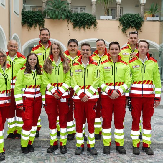 Eine Gruppe von Menschen in Sicherheitsuniformen steht vor einem Gebäude. Sie lächeln für ein Foto.