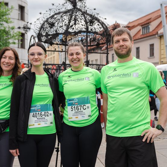 Vier Personen tragen passende grüne T-Shirts mit dem Wort Breitenfeld. Sie posieren für ein Foto bei einer Outdoor-Veranstaltung. Eine Frau links trägt eine schwarze Jacke und eine Brille.