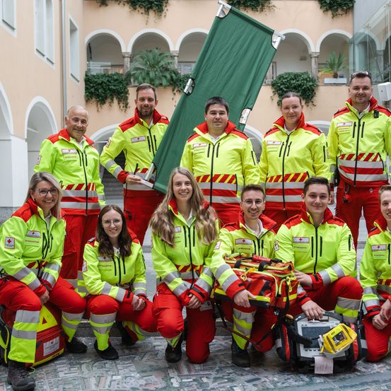 Eine Gruppe von Rettungssanitätern und Rettungsassistenten in gelben und roten Uniformen posiert für ein Foto vor einem Gebäude.