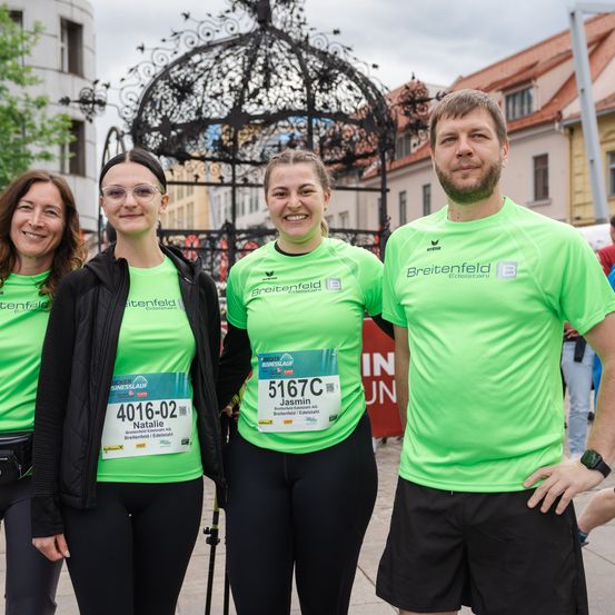 Vier Menschen in grünen T-Shirts mit dem Wort Breitenfeld posieren für ein Foto draußen. Dahinter steht ein Gebäude mit einem Baum davor.
