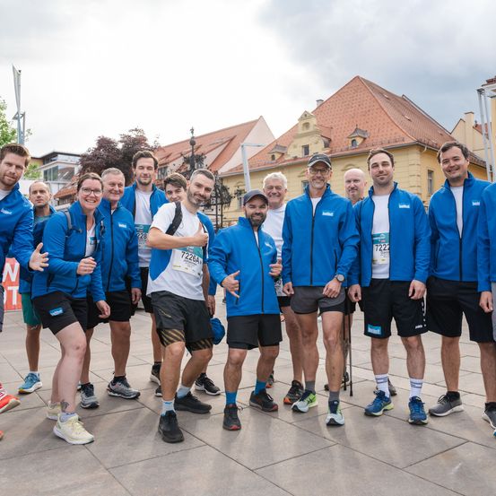 Eine Gruppe von Männern in passenden blauen Jacken und Turnschuhen posiert für ein Foto vor einem historischen Gebäude.