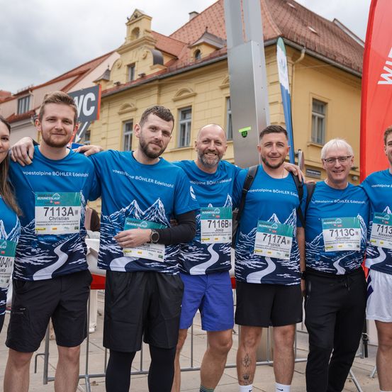 Eine Gruppe von Läufern in passenden blauen T-Shirts posiert für ein Foto an der Startlinie eines Marathons mit einer Stadtlandschaft im Hintergrund.