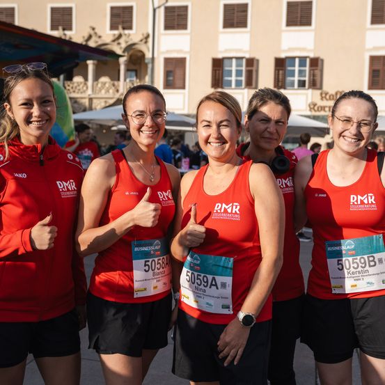 Fünf Frauen in roten Shirts stehen lächelnd zusammen. Sie tragen Laufnummern mit den Nummern 5058A, 5059A, 5059B, 5058A und 5059A. Sie nehmen wahrscheinlich an einem Marathon teil.