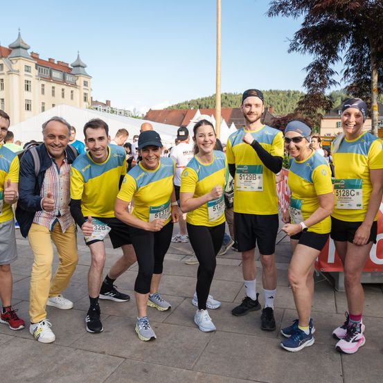 Eine Gruppe von Menschen in gelber und blauer Laufausrüstung, wahrscheinlich bei einem Marathon, posiert sonnig für ein Foto.