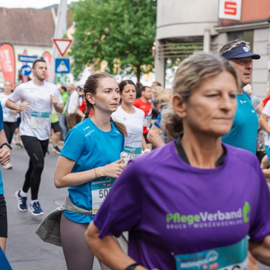 Ein Marathon mit Läufern in verschieden farbigen Shirts, eine trägt ein blaues Shirt mit der Nummer 50, eine andere ein lila Shirt mit einem Logo.