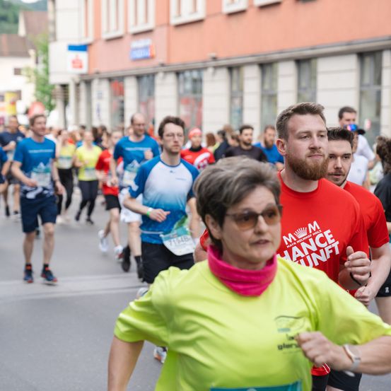 Teilnehmer eines Marathonrennens, mit einer Frau in Grün im Vordergrund und einem bärtigen Mann in Rot hinter ihr.