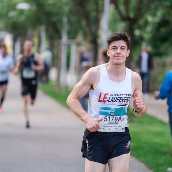 Ein junger Mann läuft in einem Marathon und trägt ein weißes Tanktop mit dem Text Future Team Le-Laufevent. Er ist in Führung.